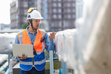 İnşaat alanındaki çatı havalandırması ya da boru sistemini incelerken telsiz ve dizüstü bilgisayar kullanarak güvenlik donanımı mühendisi, düzgün kurulum, güvenlik ve işletim standartları sağlanıyor.