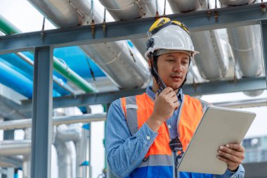 Fabrikadaki ekipman denetimi ve izleme için tablet ve telsiz kullanan sanayi mühendisi, güvenlik, verimlilik ve dijital operasyon yönetimine odaklanıyor.