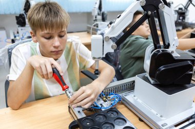 Genç bir öğrenci laboratuvar ortamında robot kolu monte ediyor. STEM eğitimi kavramı, robotik gençlik, öğrenme, geleceğin mühendisleri ve otomasyon teknolojisine erken maruz kalma.