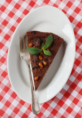 Bir parça çikolatalı kek, tipik İsviçre pastası, masada beyaz bir tabakta, fındık ve nane ile süslenmiş.