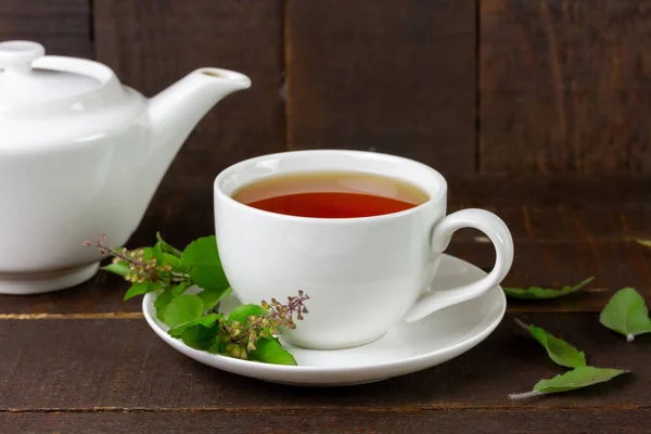 Tulsi or holy basil tea in white cup with fresh tulsi leaf on wooden background. Ayurvedic medicine in India.