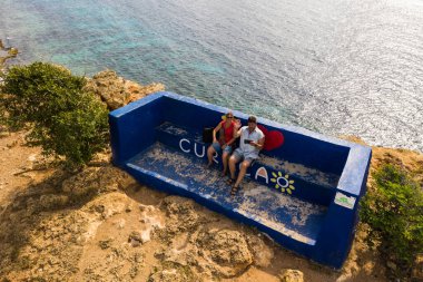 Çift arka planda deniz olan bir bankta oturuyor. 