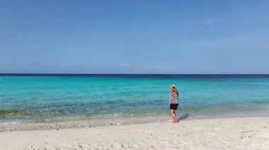 Karayipler 'deki tropikal bir adada beyaz plajda yürüyen bir kadın.