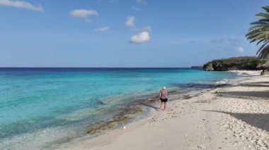 Karayipler 'deki tropikal bir adada beyaz plajda yürüyen bir kadın.