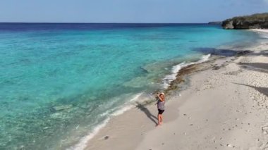 Karayipler 'deki tropikal bir adada beyaz plajda yürüyen bir kadın.