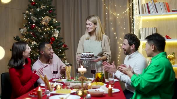 休日のクリスマスディナーとお祝いのコンセプトを持つ幸せな友人の多民族グループの人々主婦は夜のテーブルの再会パーティーでベーキング皿を準備し 提供しています — ストック動画
