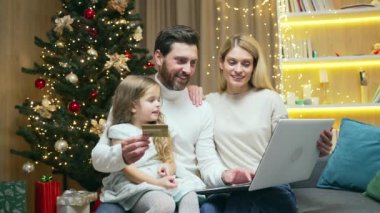 Çocuklu bir aile internet üzerinden dizüstü bilgisayar ve kredi kartı alışverişi kullanarak online alışveriş yapıyor. Noel hediyesi al ve yeni yıl tatilinde hediye al.