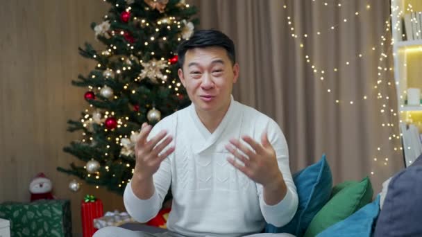 亚洲男子在网上观看摄像机时 向朋友们致以圣诞快乐和新年快乐的祝愿 祝贺在家里的圣诞树的远程摄像头视图背景 — 图库视频影像