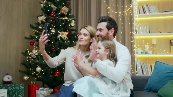 幸せな家族男性女性と女の子子供はビデオ会議チャットを介してリモートでお祝いを通信オンライントークメリークリスマスとハッピー新年自宅でスマートフォンを使用して — ストック動画