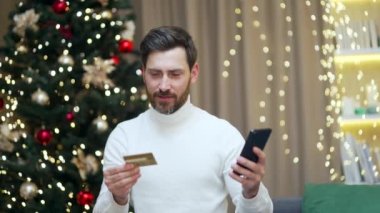 Mutlu adam internetten cep telefonu ve kredi kartı kullanarak alışveriş yapıyor. Yılbaşı tatillerinde evde oturuyor. Hediye olarak kanepeye oturuyor.