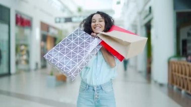 Satış ve indirimlerden sonra alışveriş merkezinden alışveriş yapan mutlu İspanyol kadının portresi. Renkli hediye çantalarıyla gülümseyen ve içeriden memnun bir kız satın alan kameraya bakıyor.