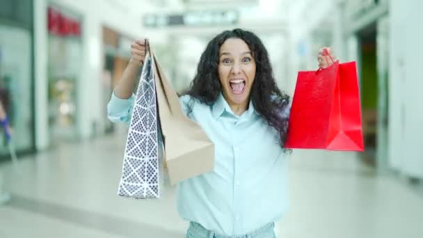 ポートレートクレイジー若いお店の女性は幸せな幸せな幸せなショッピングモールセンターでジャンプを喜びます販売後割引見てカメラ喜び笑顔でギフトバッグで購入満足ワンダーガール — ストック動画