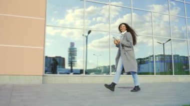 Kentin arka sokaklarında gezen güzel İspanyol bir kadın akıllı cep telefonu ve kahve fincanıyla hayatın tadını çıkarıyor. Gri montlu kız dışarıda mutluluk dolu bir hayat sürüyor.