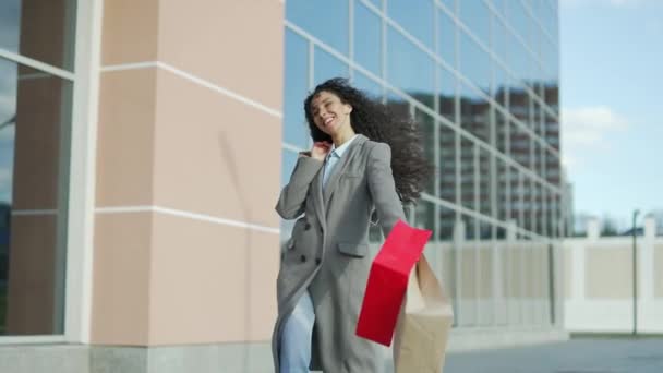 幸せな陽気な若いヒスパニック系の女性はギフトペーパーバッグで買い物をした後に行きます 屋外モールで満足した女性スマイリングは 現代のセンターセールスーパーマーケットを背景に歩いています ブラックフライデーの幸せ — ストック動画