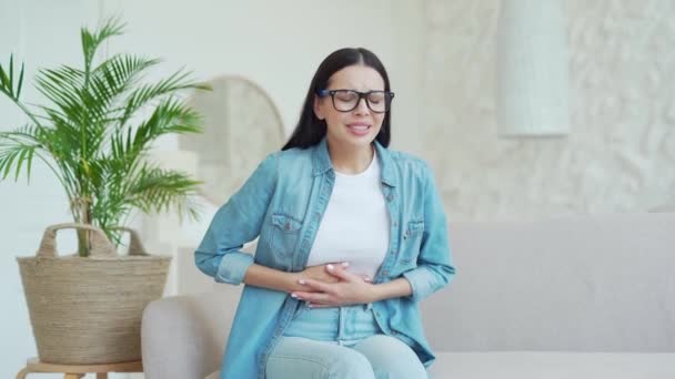 Chora Ciemnowłosa Kobieta Okularach Cierpiąca Ból Brzucha Siedząca Kanapie Trzymająca — Wideo stockowe