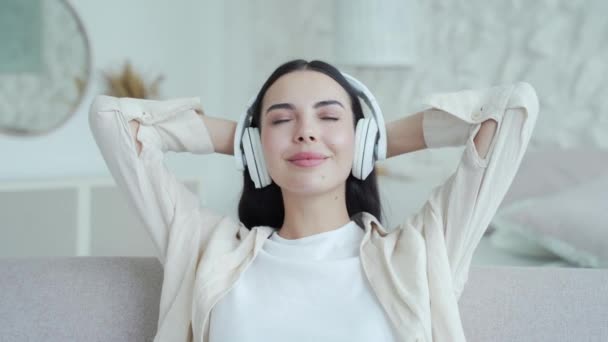Vonzó Barna Fülhallgatóval Zenét Hallgatni Kényelmes Kanapén Világos Nappaliban Mosolygó — Stock videók