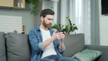 Evde akıllı telefondan rahatsız olan sinirli, genç sakallı bir adam. Stresli erkek cep telefonu kullanırken sinyal kaybı yok. Uygulamada hata yok. Kötü servis kavramı