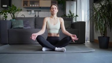 Sakin sakin kadın, nilüfer pozisyonunda oturmuş, yavaş yavaş meditasyon yapıyor ve nefes alıyor. Oturma odasında yoga yaparken, atletik gözleri kapalı kadın, evde meditasyon yapıyor. Stres kavramı yok.