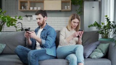 Evli genç çift, arka arkaya kanepede oturup yazışıyorlar sosyal ağda akıllı telefonlarda yazışıyorlar karı koca birbirlerini yokluyorlar evliliğe olan güven kavramını görmezden geliyorlar.