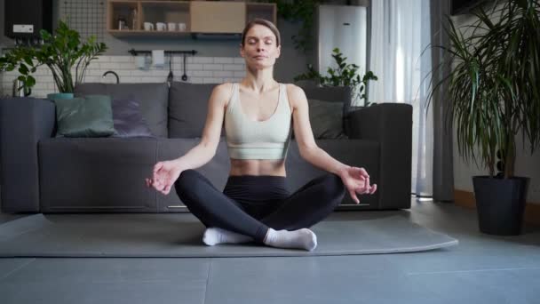 在客厅里做瑜伽时 放松的女人坐在荷花的位置上沉思 慢慢地呼吸 同时在客厅里做瑜伽 运动女性闭目养神在家做冥想练习没有压力概念 — 图库视频影像