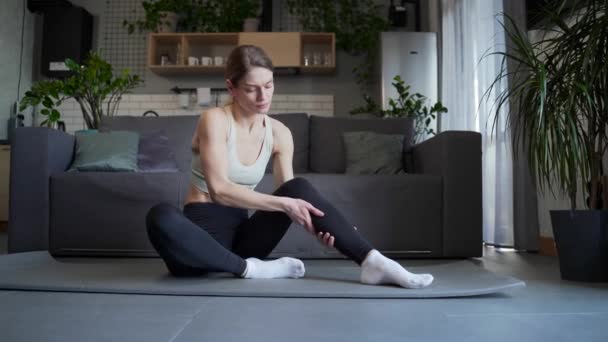 可悲的女人在运动锻炼和在客厅的垫子上做按摩后 突然感到腿疼 独自在家健身会使有健康问题的女人心烦意乱 — 图库视频影像
