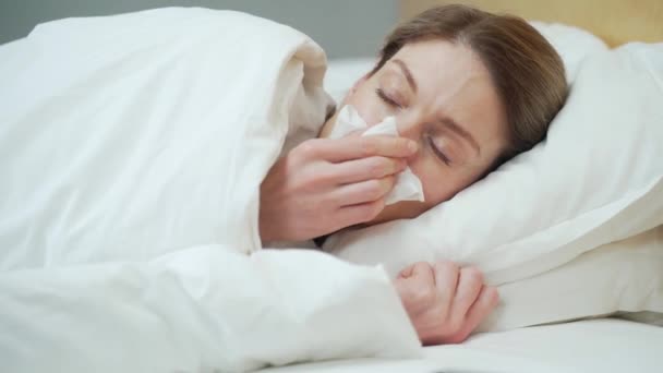 病気若いですブロンド女性吹いて実行鼻くしゃみと咳ベッドルームで暖かいベッドの上に寝そべっています不健康な女性下ザ毛布取得インフルエンザウイルス症状寒さと熱の概念 — ストック動画