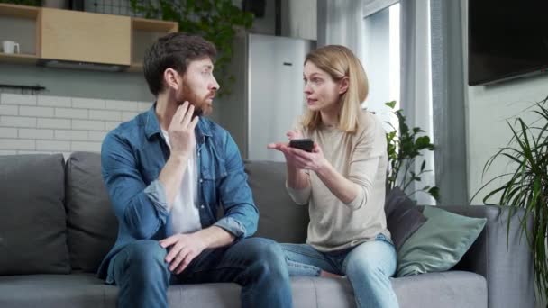 興奮した若い女性は彼を打つ夫の電話で不貞のメッセージを見つけ 彼の妻は彼を叫んでいる間に困惑した髭の男を説明するために要求しますチート嘘の概念 — ストック動画