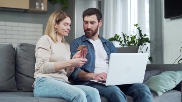 若い夫婦とクレジットカードのショッピングオンラインで請求書を支払うか 自宅でソファに座ってラップトップを使用して食品配達を注文しますインターネットで購入し コンピュータ上で支払いをする幸せな家族 — ストック動画