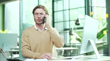 Modern ofisin içinde cep telefonuyla konuşan kendinden emin, genç bir işadamı. Yakışıklı, sakallı bir ofis çalışanı. İş yerinde akıllı telefondan profesyonel sohbetler yapıyor.