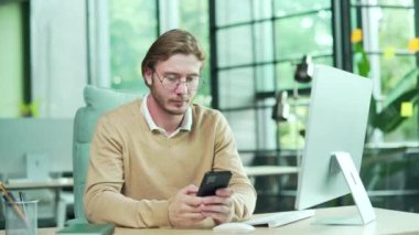 Modern işyerindeki cep telefonuyla mesajını okuduktan sonra çok mutlu bir ofis çalışanı. Heyecanlı bir çalışan ekrana bakıyor ve mutlu bir şekilde akıllı telefondan harika haberler alıyor.