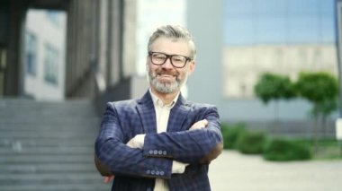 Modern iş merkezindeki kameraya çapraz kollu, kendinden emin bir iş adamı portresi. Açık ofis binalarında gözlüklü, klasik takım elbiseli başarılı bir son sınıf öğrencisi.