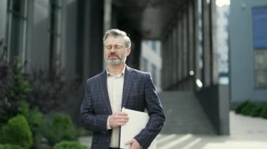 Klasik takım elbiseli, sakallı, kendinden emin bir üniversite profesörü, derslerden sonra dışarıda yürüyor. Modern eğitim binalarının yakınındaki yoğun çalışma gününden sonra, elinde laptop ve öğrenci sınavları var. 