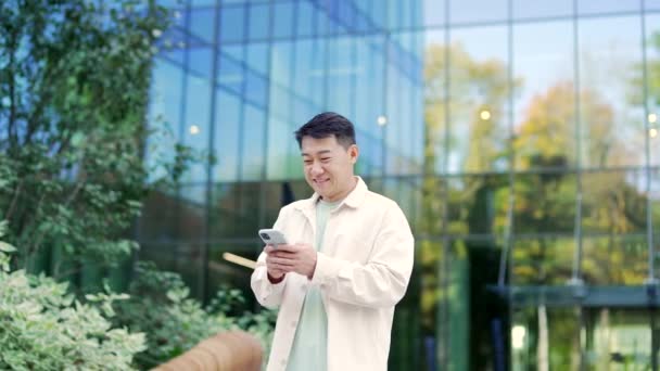 Uśmiechnięty Młody Pozytywny Azjatycki Mężczyzna Trzymać Smartfon Przewijanie Oglądanie Social — Wideo stockowe