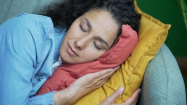 Rahat gülümseyen genç bir kadının yakın portresi. Oturma odasındaki kanepede güzel hayallerle uyuyan koyu renk saçlı kıvırcık kız. Evdeki rahat kanepede dinleniyor.