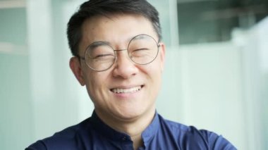 Modern ofisteki kameraya bakan gülümseyen bilişim uzmanı portresi. Yalnız başına geliştirme şirketinde çalışan Asyalı girişimci profesyonel girişimcinin resmi.