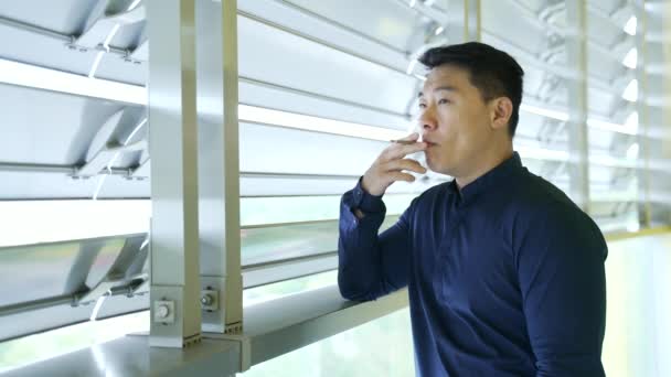 職場での休憩中にアジアのビジネスマンの喫煙を自信を持って単独で職場で休憩中に青のシャツの魅力的な起業家の男の肖像屋内近代的なオフィスビルのリラックスビジネスライフスタイル — ストック動画