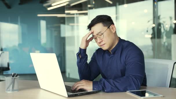 不幸なアジアのItプログラマー頭痛の種痛みを伴う感情慢性片頭痛オフィスのコンピュータで働く高または低気圧ストレスを受けた起業家は屋内の職場で怪我を感じています — ストック動画