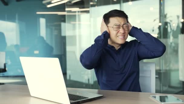 Zestresowany Azjatycki Przedsiębiorca Pracujący Laptopie Zakrywający Uszy Dłońmi Wkurzonymi Hałaśliwymi — Wideo stockowe