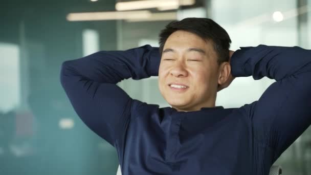 頭の後ろの手で笑顔アジアのItプログラマーの従業員は 仕事に満足していますよくやった屋内ビジネスマンは ハードワークの日が終了した後リラックスコーディングプロジェクトや現代の職場での書類作成 — ストック動画