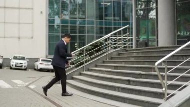 Klasik takım elbiseli başarılı iş adamının arkası. Modern iş merkezindeki sohbetle akıllı telefon tut. Ofis binalarının merdivenlerini çıkarken acele et.