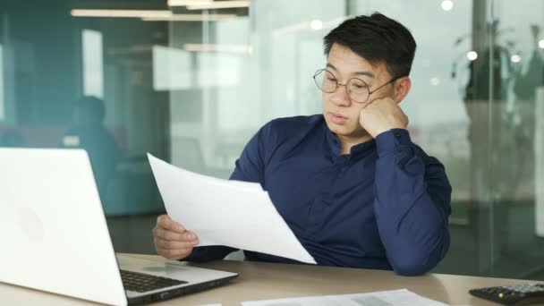 疲れて過労のアジアのビジネスマンItプログラマーは 現代のオフィスで紙の作業文書に問題があります開発会社のデータを分析する統計レポートで疲れストレスを感じる男 — ストック動画