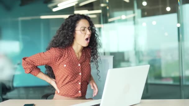 若いヒスパニック系の女性が職場で腰痛になった オフィスのコンピュータデスクで長い間座っている女性の腰痛屋内従業員の起業家は 低緊張で痛みに苦しんでいます — ストック動画