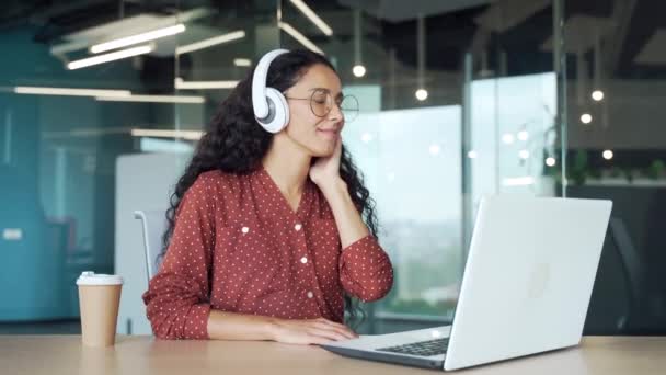 現代オフィスでノートパソコンやヘッドフォンで音楽やラジオを聞いて作業している現在 パニックブルネットの若い女性従業員快適な女の子学生労働者は屋内で職場で楽しんで — ストック動画