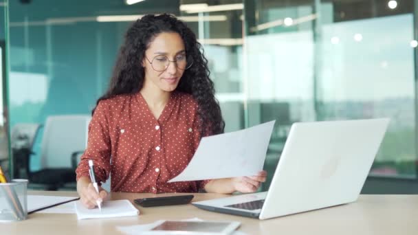 年轻的拉丁裔美国女会计办事员在工作场所处理办公室文件 忙着做纸质计算财务报告 使用个人电脑笔记本电脑 女雇员企业家 — 图库视频影像
