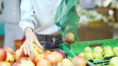 Genç kadınların ellerini kapatarak sebze ya da meyve dolu eko poşetlerin içine sebze ya da meyve koyuyor. Marketteki Kadın Markette Duruyor. Tezgahta Yeniden Kullanılabilir Paket Kullanıyor.