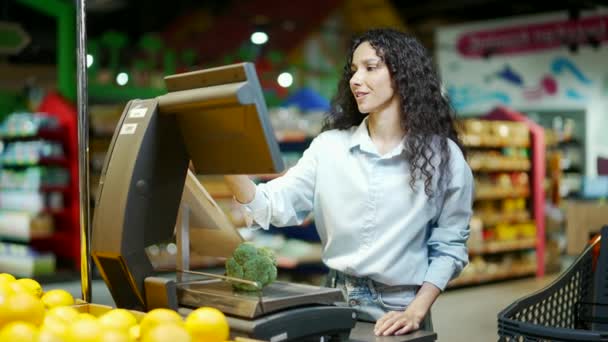 若いかなりブルネットの女性の買い物客はスーパーマーケットの食料品店で食料品の野菜を量ります女性の顧客やバイヤーは 食品市場でのスケールで毎日の購入を行います製品の計量とセルフサービス — ストック動画