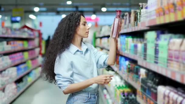 女性は スーパーマーケットで化粧品ボトルにシャンプー女性の顧客読書ラベル上の製品の組成を調べます 研究と情報を読み取る考慮事項は店内で選択を行います — ストック動画