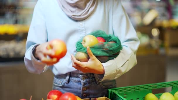 若い手の閉じる選択し スーパーマーケットのリンゴの野菜や果物のエコバッグにピックを置きますカウンターで食料品店に立つ女性は 市場閉鎖で再利用可能なパッケージを購入します — ストック動画