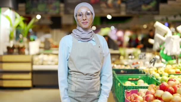 腕を組んで笑顔立って野菜のセクションのスーパーマーケットでヒジャーブ労働者の肖像イスラム教徒の女性が交差した 果物屋の市場でカメラを見て優しい快適な女性従業員作業エプロンで — ストック動画