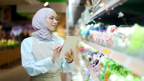 在超市 杂货店或围裙店工作的穆斯林妇女与数码平板电脑女经理小企业主雇员检查货架库存品 — 图库视频影像